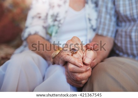 Cropped shot of elderly couple holding hands while sitting together at home. Focus on hands. Royalty-Free Stock Photo #421367545