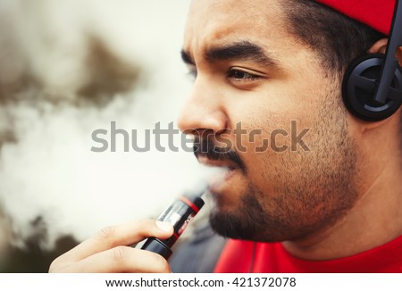 Vaper black guy. Portrait of vaping african male. Young adult person smoking electronic cigarette with propylen glycol vape juice. Dark skinned man smokes ecig and exhales vape smoke
