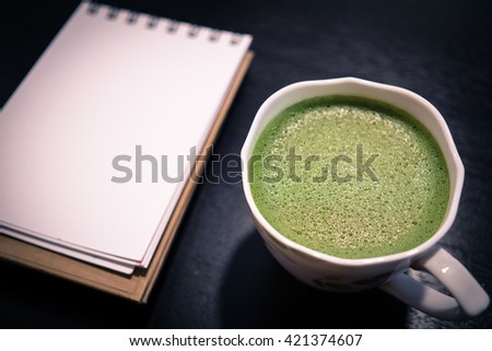 Close-up cup of hot green tea with open notebook