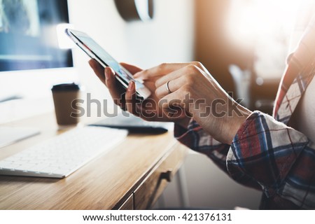 Close-up of female hands using smart phone while working on computer at modern office interior, businesswoman typing text message on her cellphone at loft interior, flare light, flare light