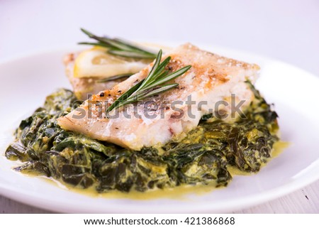 white fish fillet with herbs on fried spinach