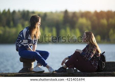 Two friends teen girls spend time together at the pier of the river.