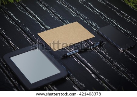 A sheet of paper, tablet and mobile phone lying on a black wooden background. It can be used for creating mock up, design, blank, wedding invitations, holidays, Valentine. Side view