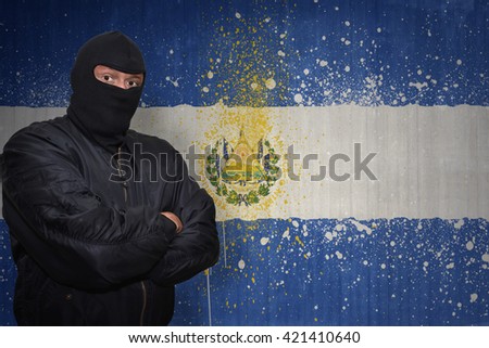 dangerous man in a mask standing near a wall with painted national flag of el salvador