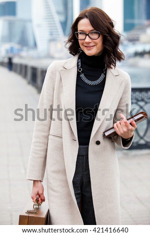 beautiful middle-aged woman in a bright coat with a wooden case and a book in their hands smiling and looking at the camera