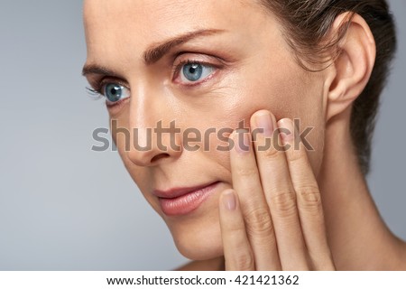 Attractive middle aged woman touching her cheek skin, mature beauty concept Royalty-Free Stock Photo #421421362