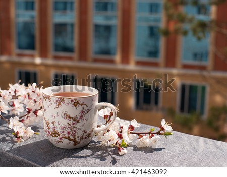 Tea in a mug with a picture of apricot. Apricot tea on the balcony window sill. Flowering branches of apricot tree create a spring mood. Tea with apricot flavor under the sun. Spring tea.