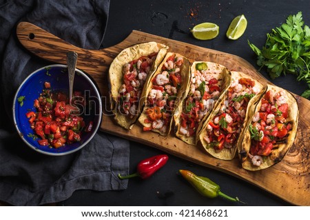Shrimp tacos with homemade salsa, limes and parsley on wooden board over dark background. Top view. Mexican cuisine Royalty-Free Stock Photo #421468621