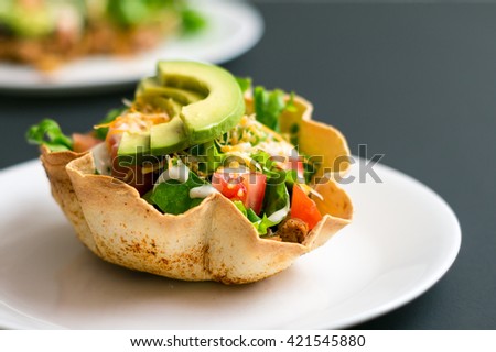 A taco salad in tortilla bowl is a fun and colorful way to eat mexican food. Made with fresh ingredients such as avocado, tomatoes, green salad, cheese and delicious sour cream vinaigrette.