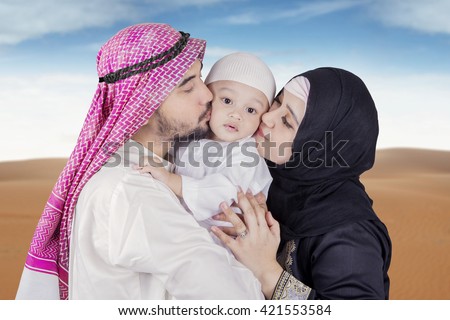 Picture of Arabic young couple wearing islamic clothes and kiss their son on the desert