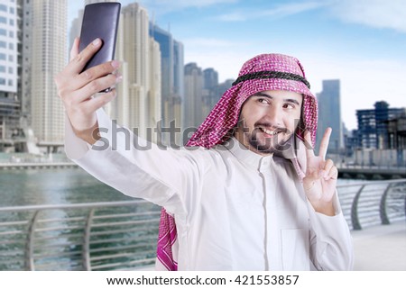 Happy Arabian person using a mobile phone to take selfie picture in the city