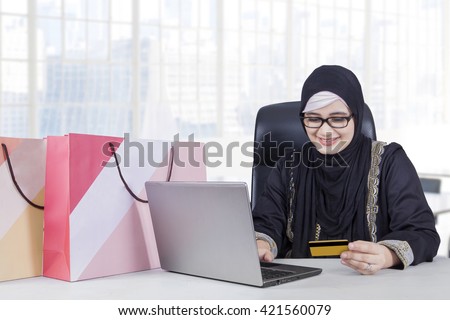 Picture of Arabic female worker using laptop and credit card for shopping online in the office
