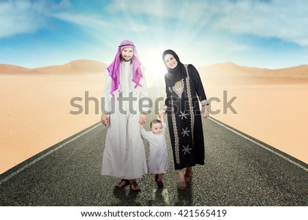 Picture of Arabic family smiling at the camera while holding hands together and walking on the street at desert