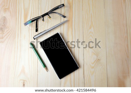 Smartphone with blank area on touchscreen with pen, glasses, pencil, USB Flash drive  on pine wood background