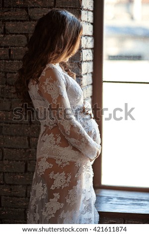 Pregnant woman in a lace dress stands by the window