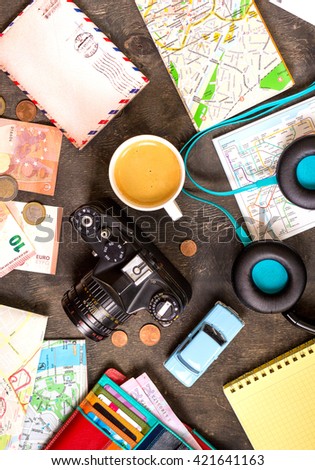 Camera, touristic maps, passport, toy car, coffee, headphones, wallet with credit cards, euro banknotes and coins on a black desk. Travel background. Tourist essentials. Plan a journey. Travel concept