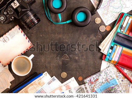 Camera, touristic maps, passport, cup of coffee, headphones, wallet with credit cards, euro banknotes and coins on the black desk. Travel background. Tourist essentials. Plan a journey. Space for text