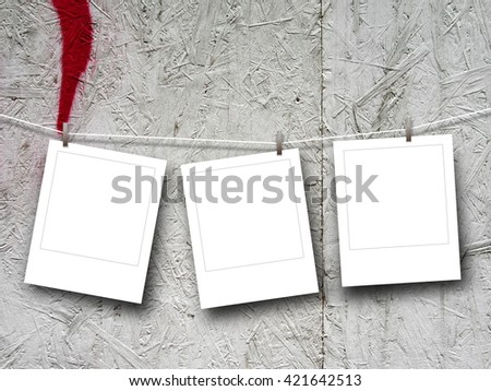 Close-up of three blank square instant photo frames hanged by pegs against painted plywood background