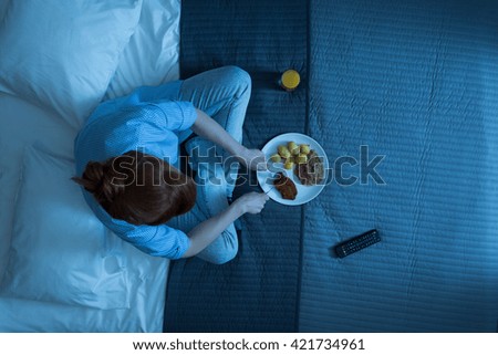 Shot of a woman sitting on a bed and eating dinner Royalty-Free Stock Photo #421734961
