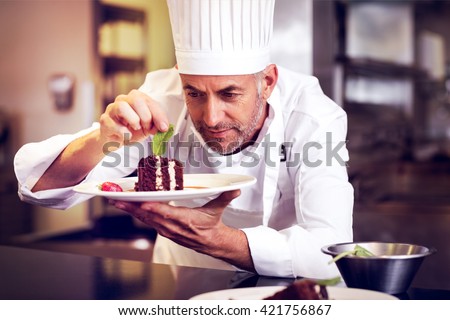 Closeup of a concentrated male pastry chef decorating dessert in the kitchen Royalty-Free Stock Photo #421756867