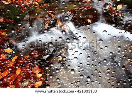 View of the autumn creek through the window glass covered by raindrops