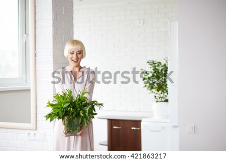 woman in a beige dress with a bouquet of mint in hand, standing on white background kitchen.