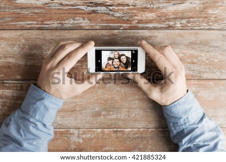 people, memory, relations and technology concept - close up of male hands holding smartphone with photo of happy friends on screen at table