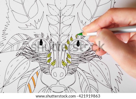 Female hand drawing with crayon in adult anti stress coloring closeup