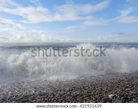Sea wave on pebble beach, blue sky with clouds