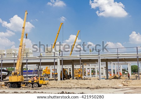 Mobile crane is loading cargo. View on construction site with machinery, people at work. 