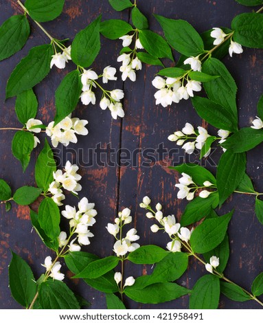 a wreath of white Jasmine flowers with green leaves on an old black wooden board with a crack. Flat lay, top view