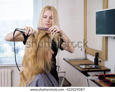 Woman barber is straightening client's long blonde hair