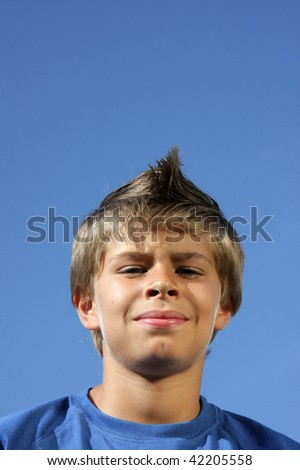 a cute smiling 10-years old boy with a fashionable hairstyle photographed in the summer sun with blue sky in the background
