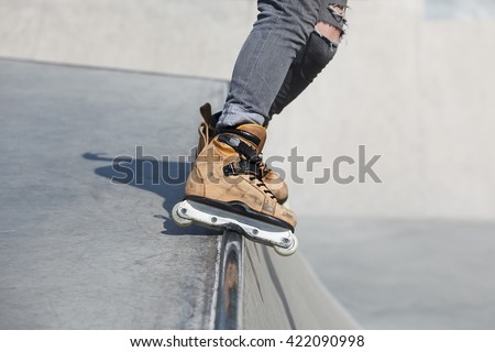 Feet of rollerblader wearing aggressive inline skates grinding on concrete ramp in outdoor skate park.Extreme sports athlete wearing roller blades for tricks and grinds grind rail in skatepark