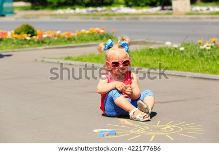 little girl drawing sun with chalks on a street