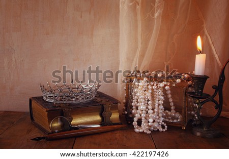 low key image of beautiful diamond queen crown, white pearls next to old book. vintage filtered. fantasy medieval period
