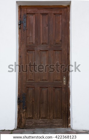 Antique wooden door. Old brown door with a decorative metal screens with a broken door handle on the front of a white concrete wall, outside