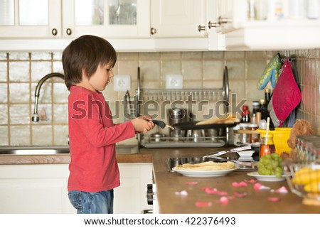 Sweet preschool child, helping his mom in the kitchen, making pancakes in the morning, happy childhood