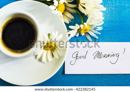 Wild daisy flowers and cup of coffee with Good morning note on rustic background