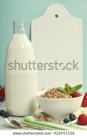 Healthy breakfast composition with a bottle of milk, berries, musli, white ceramic serving board and paper straw on white marble table with blue background, healthy eating. Space for text
