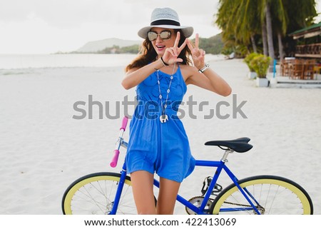 young beautiful woman with bicycle on beach, summer vacation, vintage style, bohemian outfit, blue dress, straw hat, sunglasses, smiling, happy, having fun, positive, showing peace signs with fingers