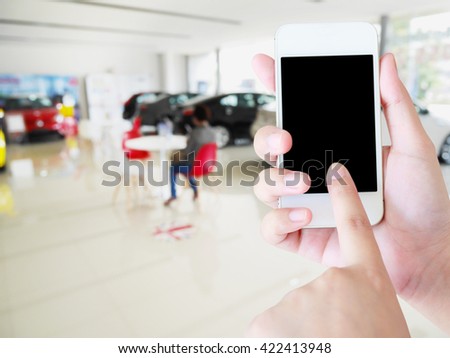 woman hands holding mobile phone with blurred background of new cars in showroom