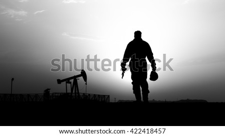 Silhouette of oilfield worker and crude oil pump in background- oilfield  - sunset - Black and white Royalty-Free Stock Photo #422418457