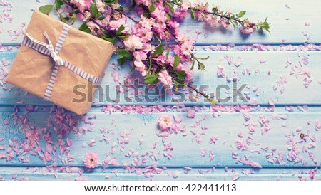 Wrapped box with present and sakura pink flowers on blue wooden planks. Selective focus. Place for text. Flat lay. Top view. Toned image.