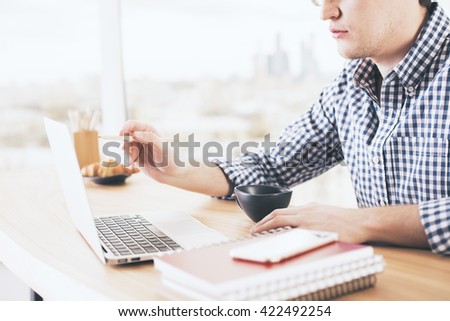 Sideview of caucasian man pointing at computer screen with pencil on blurry city background
