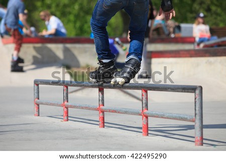 Feet of rollerblader in aggressive inline skates grinding a rail in outdoor skate park. Extreme sports athlete wearing roller blades for tricks and grinds