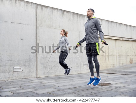 fitness, sport, people, exercising and lifestyle concept - man and woman skipping with jump rope outdoors Royalty-Free Stock Photo #422497747