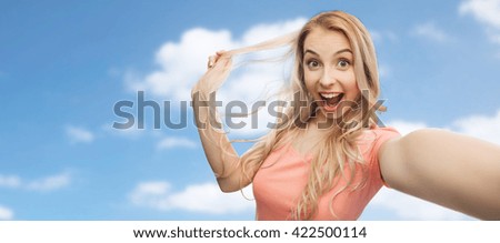 emotions, expressions and people concept - happy smiling young woman or teenage girl taking selfie over blue sky and clouds background