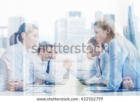 business, people, crisis and confrontation concept - smiling business team sitting on opposite sides and arm wrestling in office