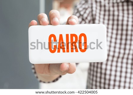 Man hand showing CAIRO word phone with  blur business man wearing plaid shirt.